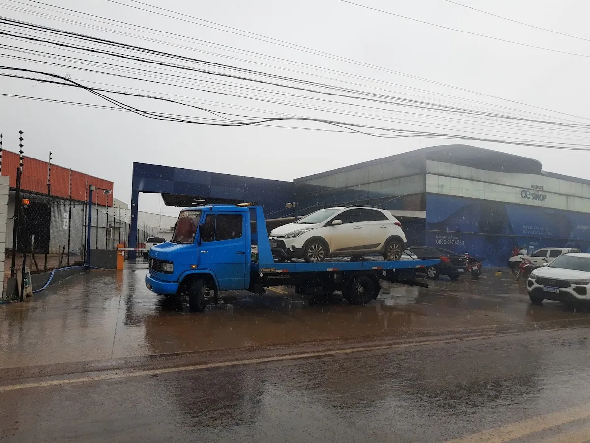 Caminhão guincho azul com um carro branco na plataforma, em dia de chuva